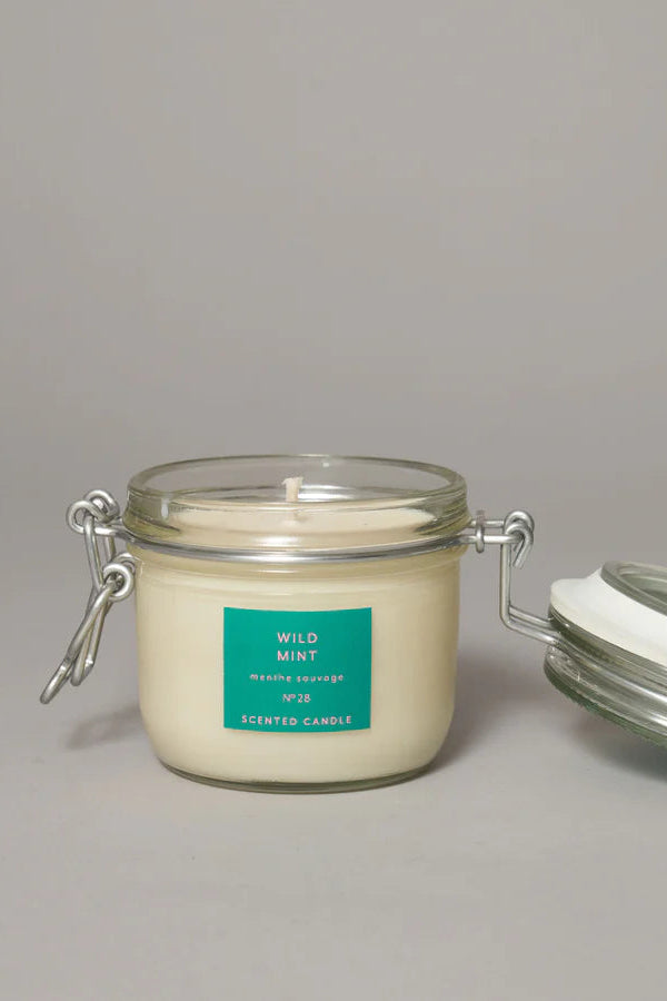 A medium-sized clear glass jar with a clip top lid containing a wild mint candle, labeled with the brand True Grace.