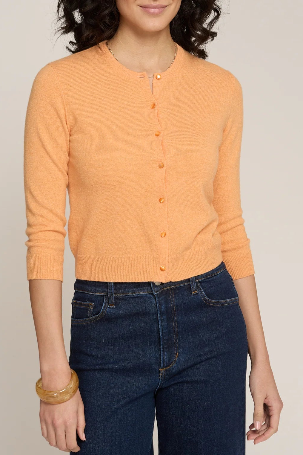 Woman wearing an orange cardigan and blue jeans against a plain background
