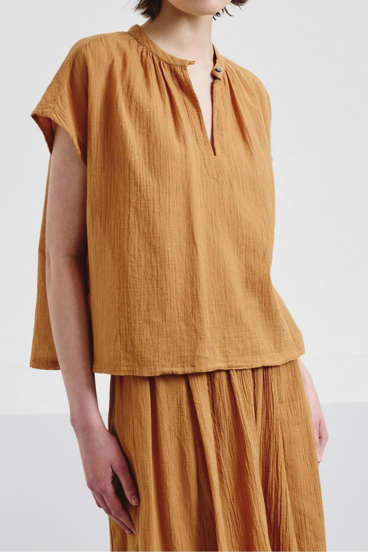 Woman wearing a mustard yellow top and skirt on a white background