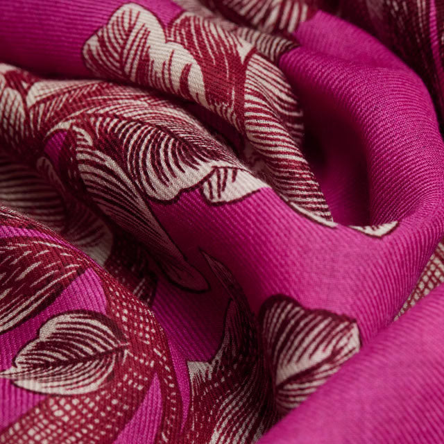 A close-up of a draped fabric with a rich magenta pink background and a detailed botanical pattern in deep burgundy and cream.