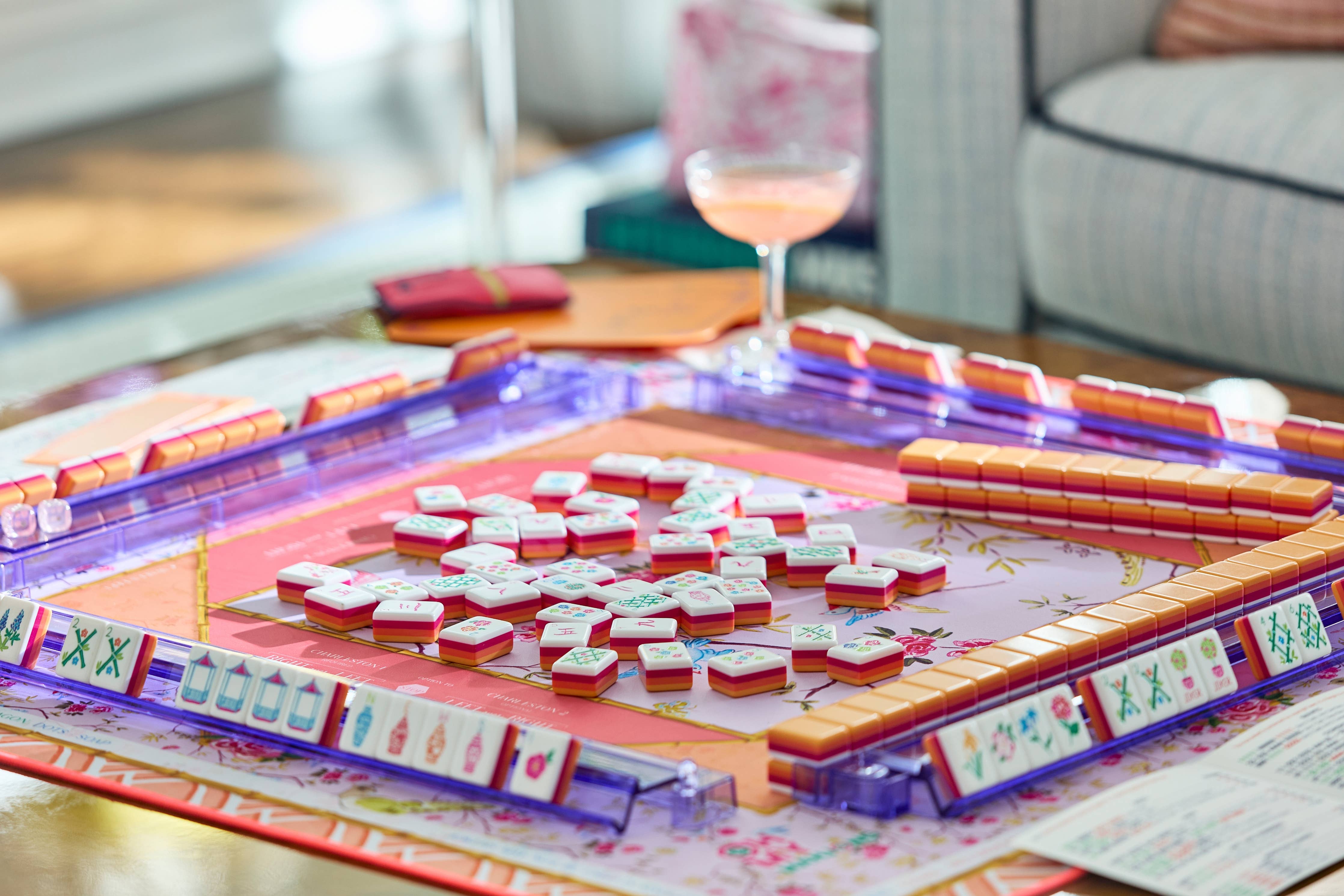 Mahjong game set on a table with a glass of pink drink in the background