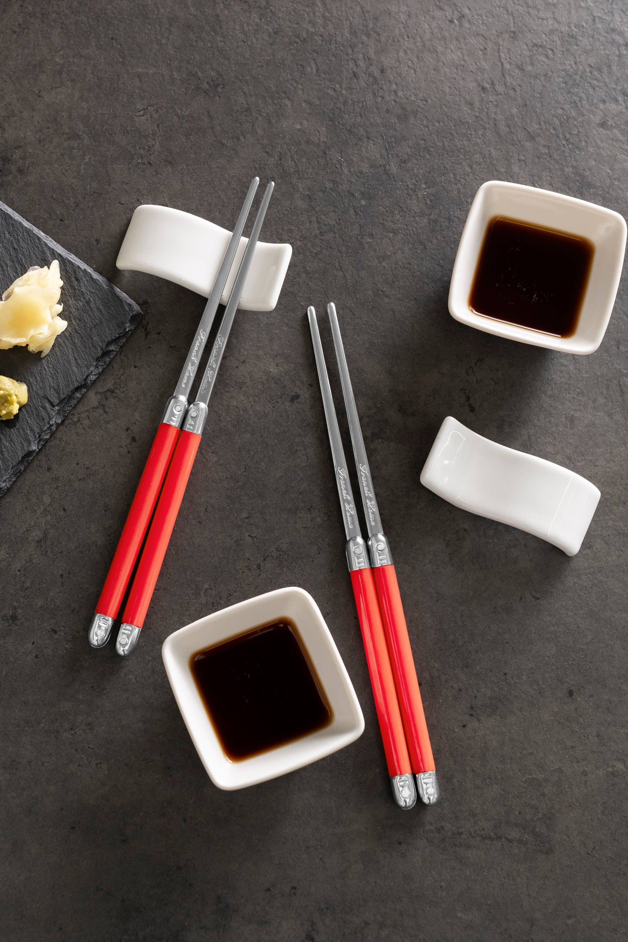 Sushi platter with red chopsticks, soy sauce, and wasabi on a dark surface