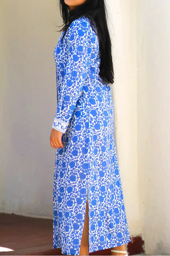 Woman wearing a blue patterned dress standing against a white wall.