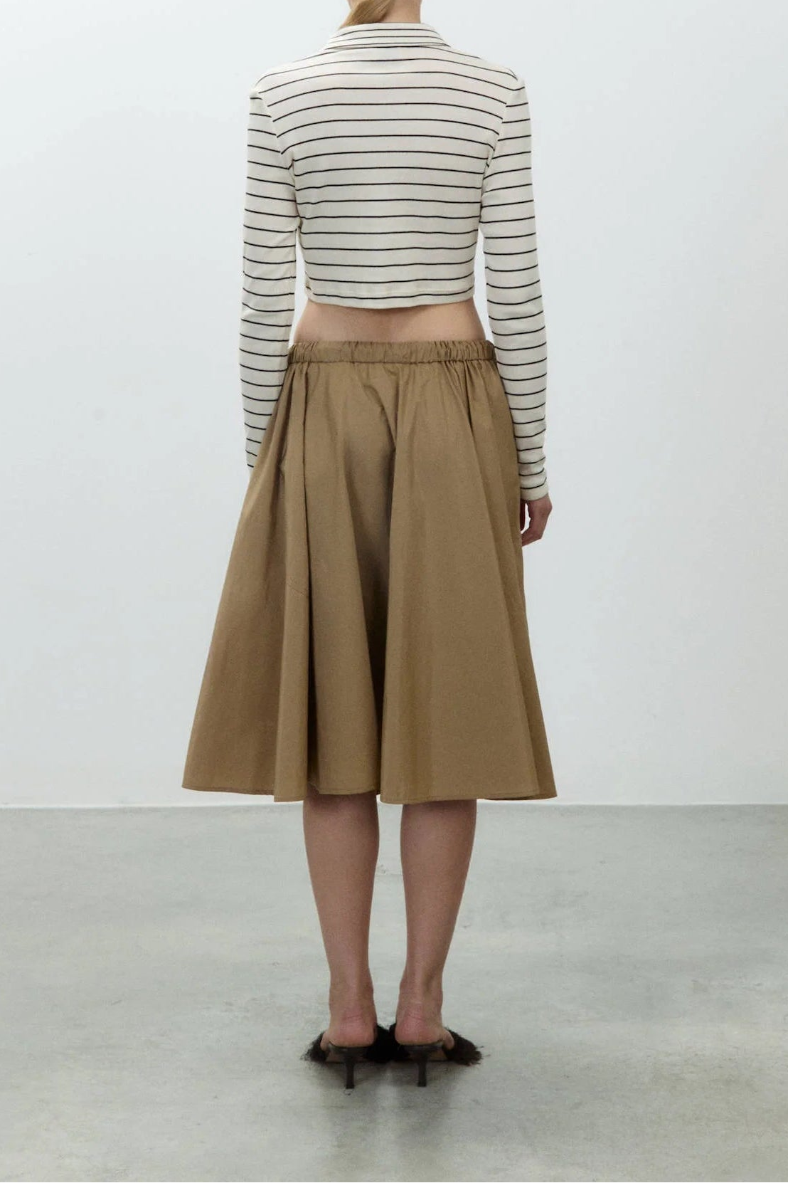Person wearing a striped shirt and beige skirt against a white background