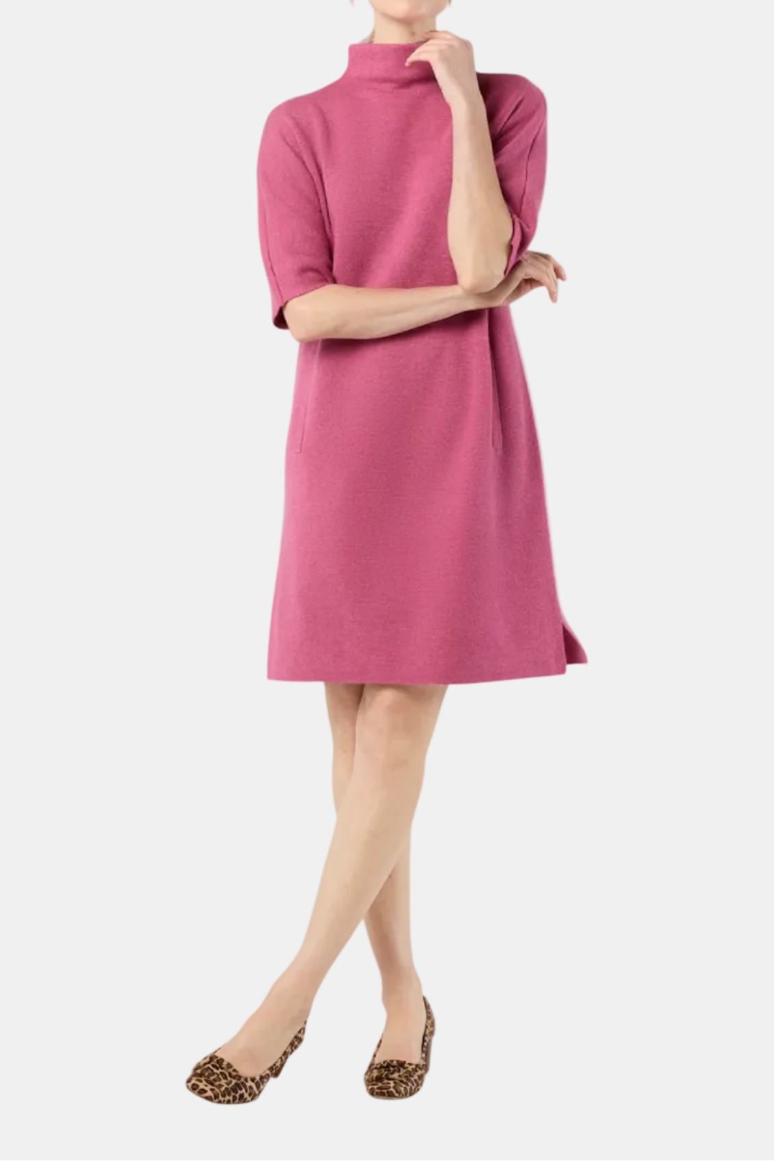 A woman modeling a short-sleeve, high-neck, knee-length knit dress in a dusty rose pink color, paired with leopard-print flats, against a solid light gray background.