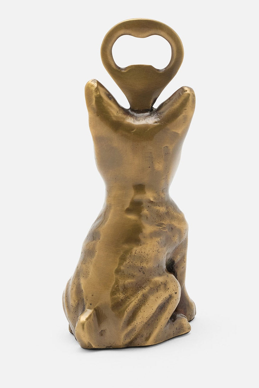 A small decorative bottle opener shaped like a seated cat, finished in a warm metallic gold/brass tone, shown against a plain light gray background.