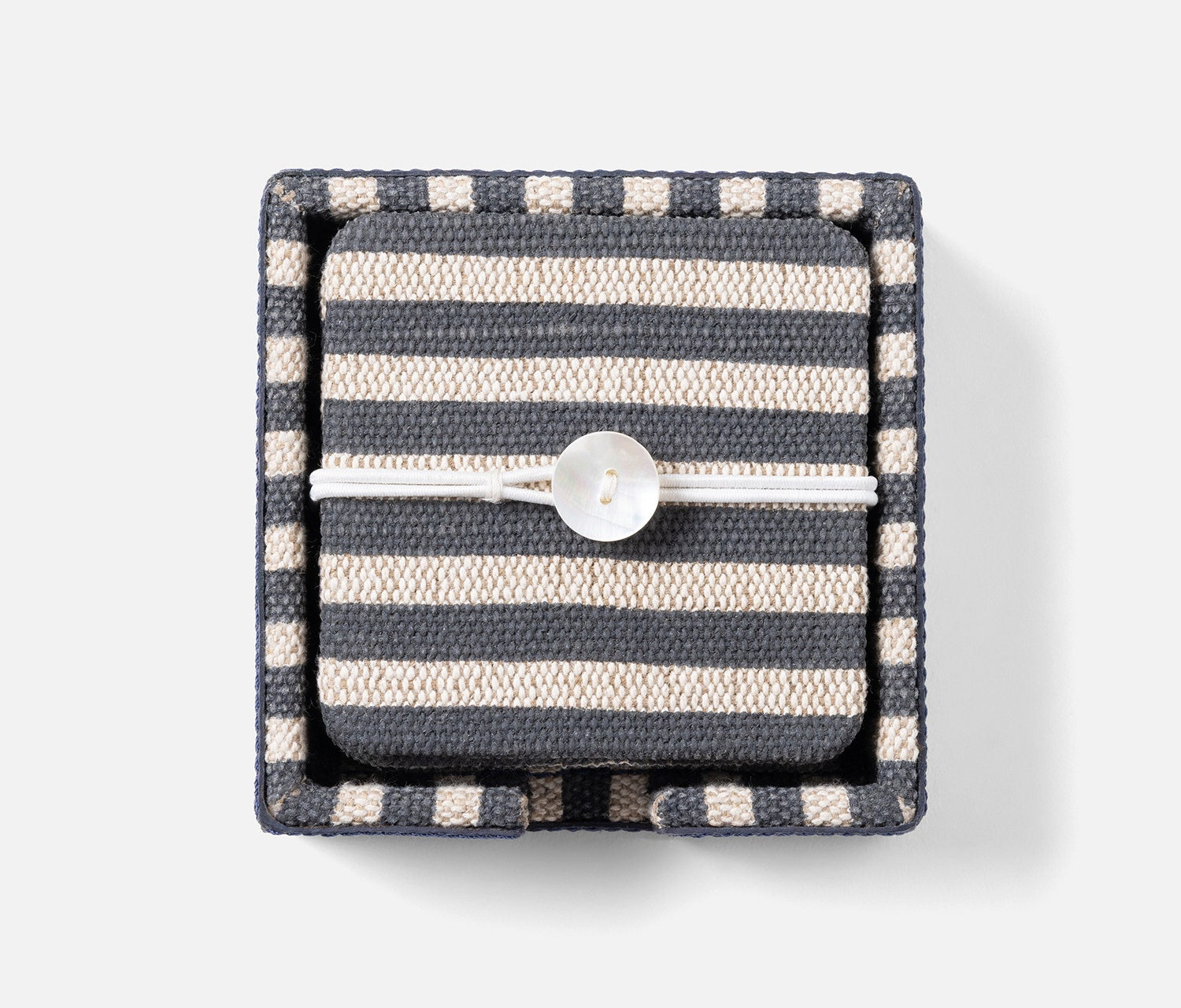 A square woven fabric jewelry box with horizontal navy and cream stripes, closed with a white elastic band and a round white button, shown on a light gray background.