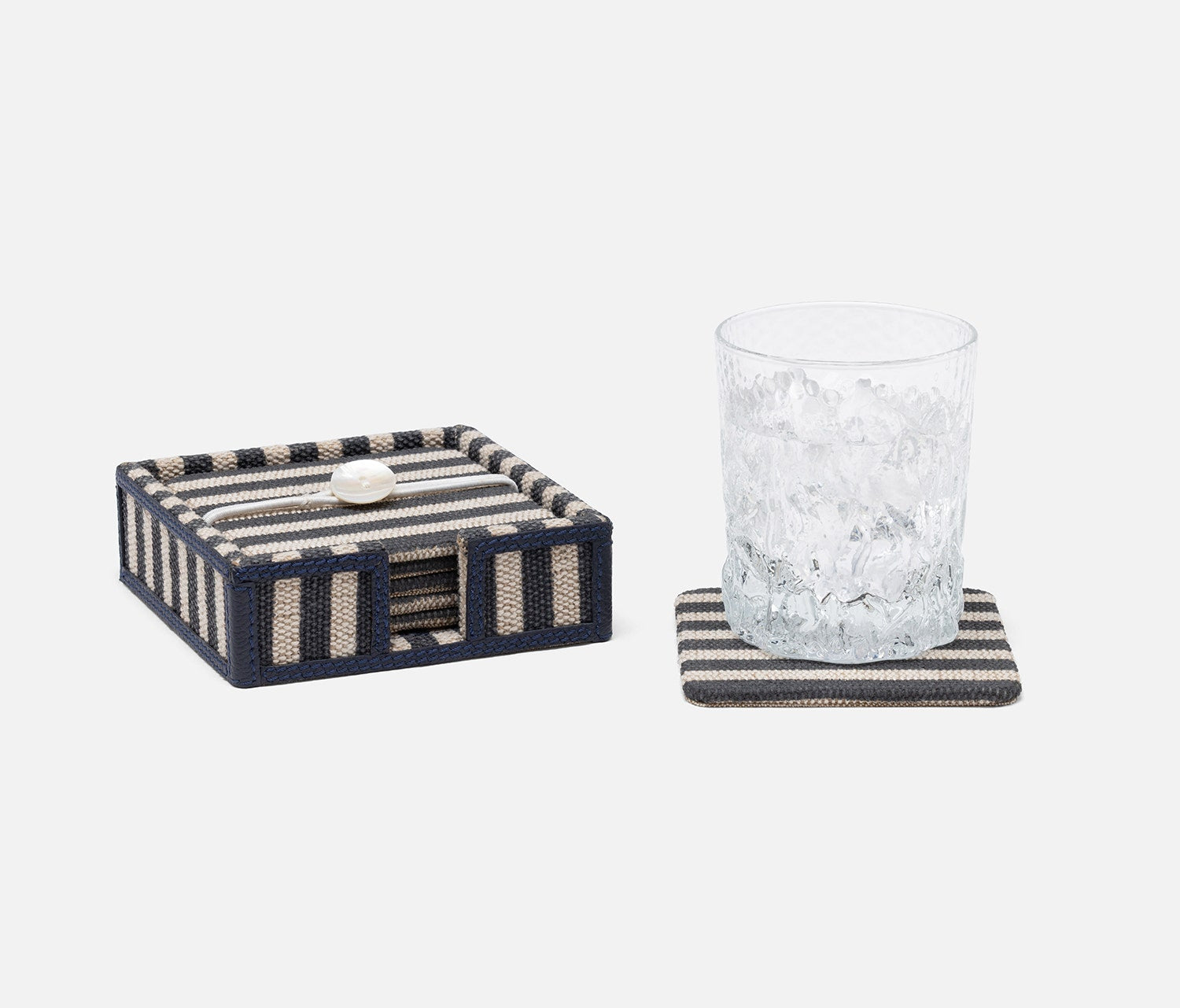 A set of striped home decor accessories including a woven box with a small white shell accent and a matching striped coaster holding a textured clear drinking glass, on a light gray background.
