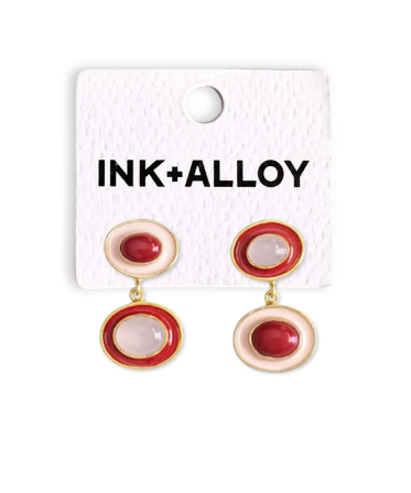 A pair of INK+ALLOY drop earrings with circular red and cream enamel details on a textured white display card.