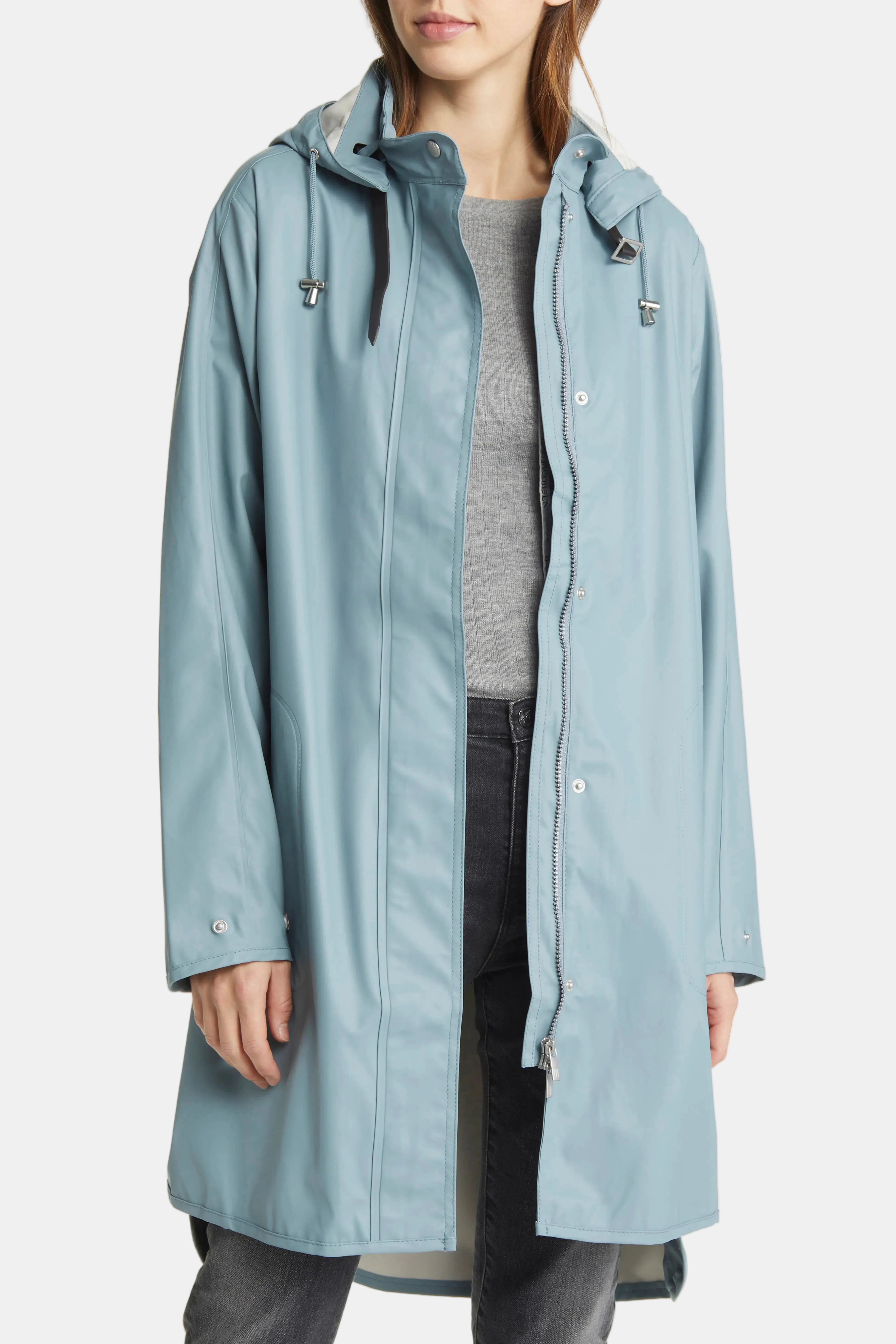 A woman wearing a light blue hooded raincoat over a gray top and dark jeans, shown from the neck down against a plain white studio background.