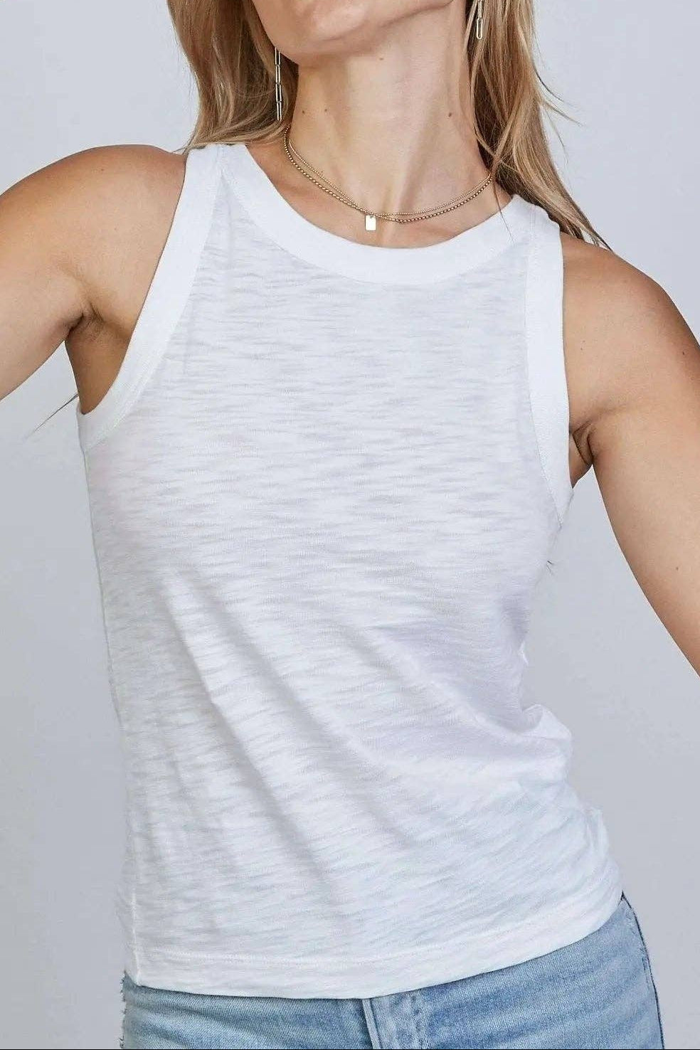 Woman wearing a white tank top and blue jeans against a plain background