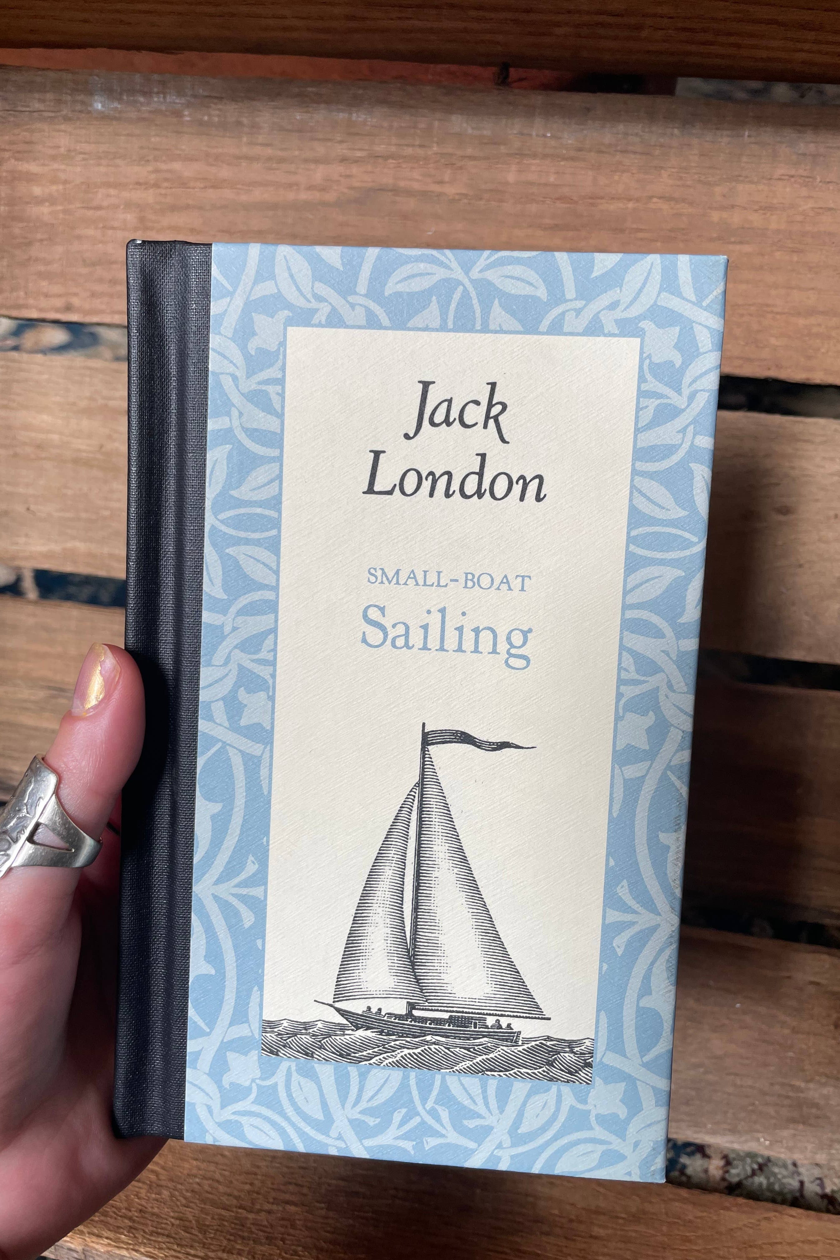Book titled 'Small-Boat Sailing' by Jack London held in a hand with a wooden background