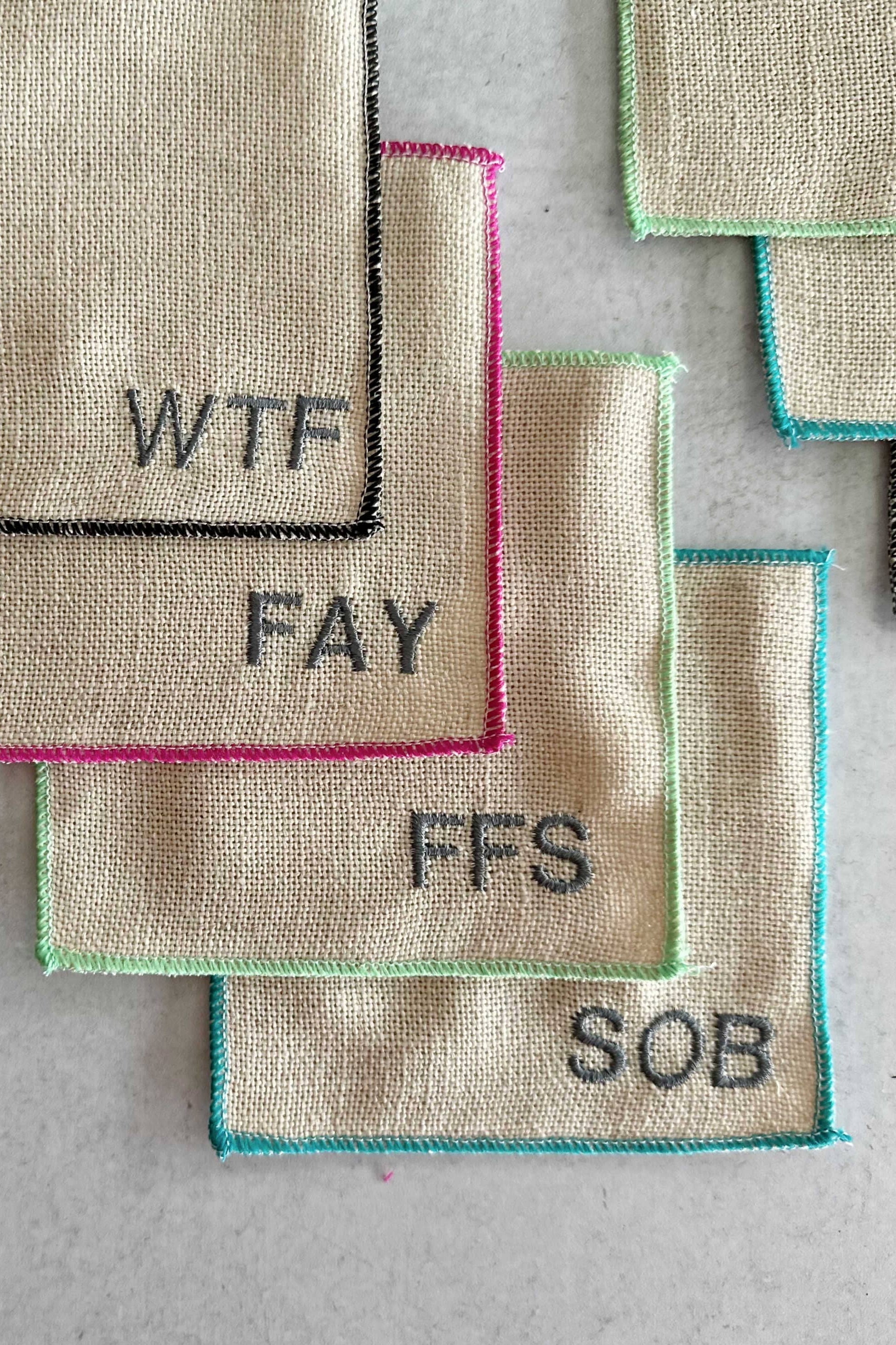 Textured fabric patches with various swear word phrases on a gray surface