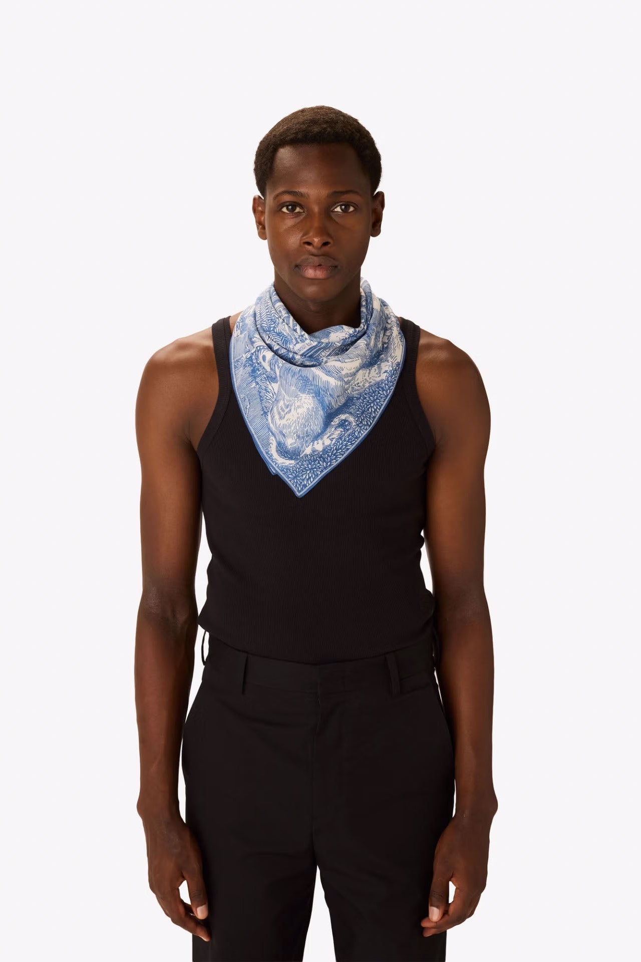Person wearing a black sleeveless top and pants with a blue patterned scarf around their neck on a white background