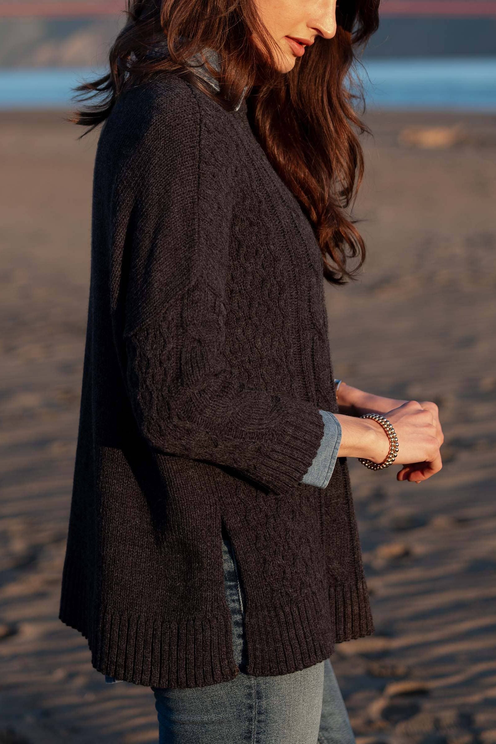 Woman wearing a dark brown cable knit sweater on a beach.