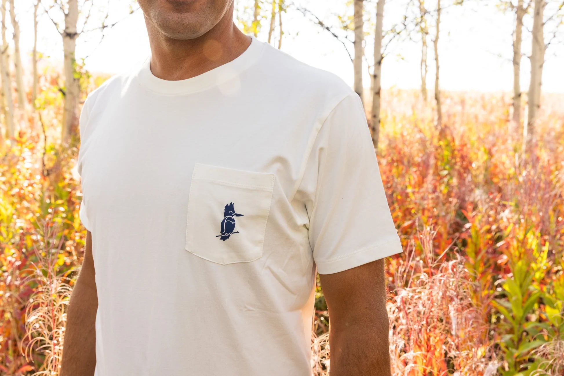 Person wearing a white t-shirt with a small logo in a natural setting