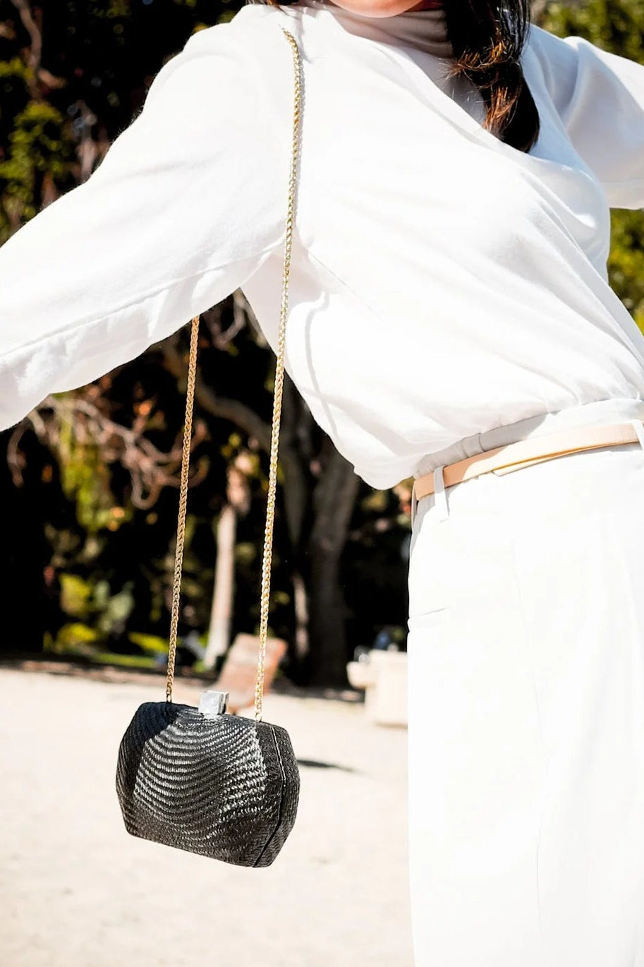 Person in white outfit holding a black handbag with a blurred outdoor background