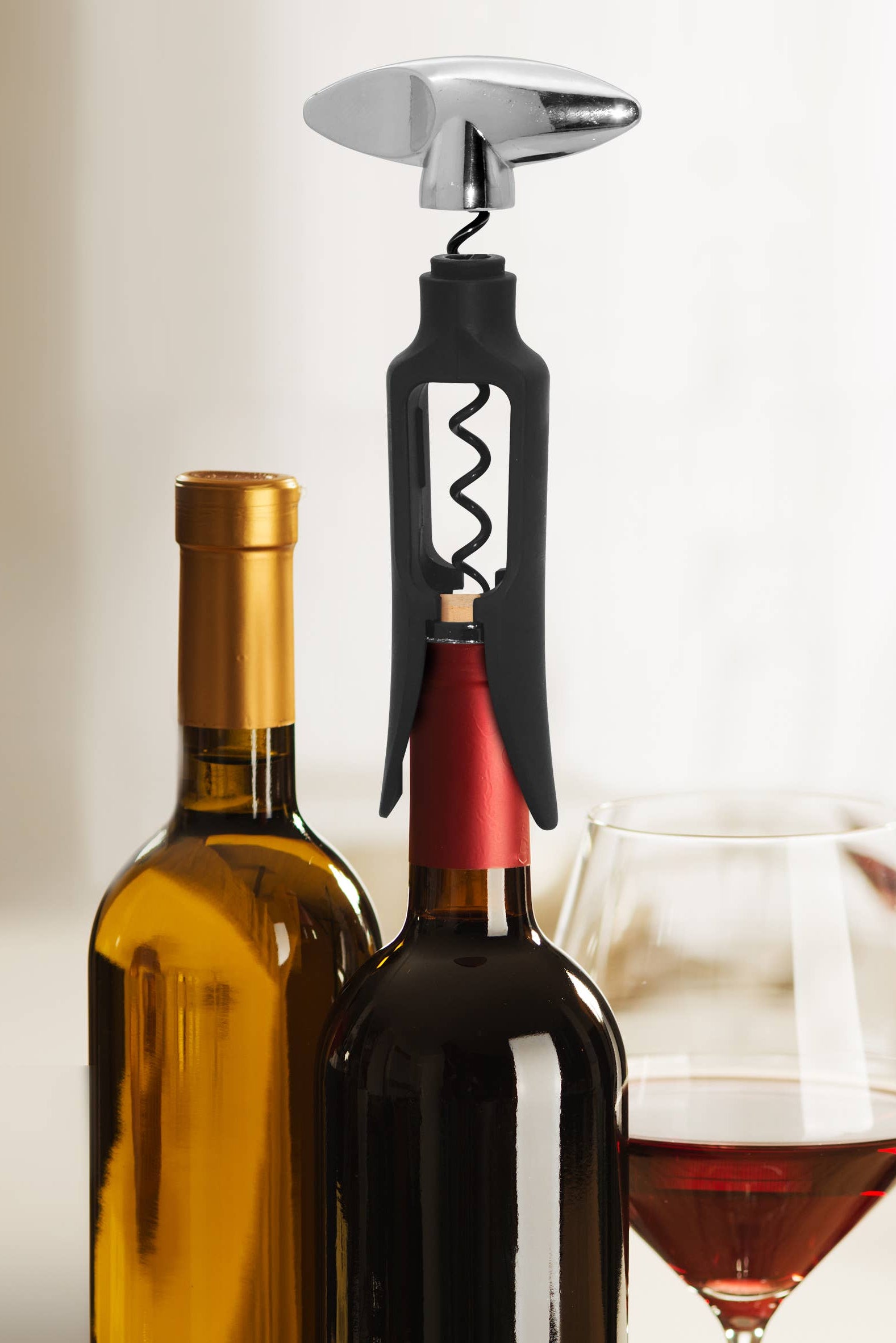 Wine bottle, corkscrew, and glass on a neutral background