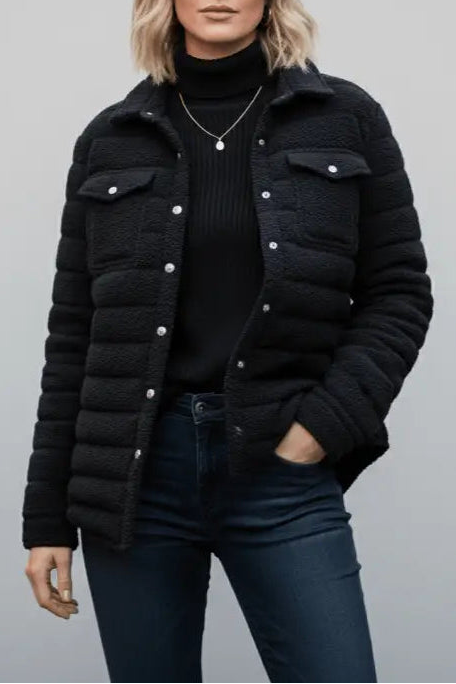 Woman wearing a black puffer jacket over a black turtleneck and jeans on a gray background