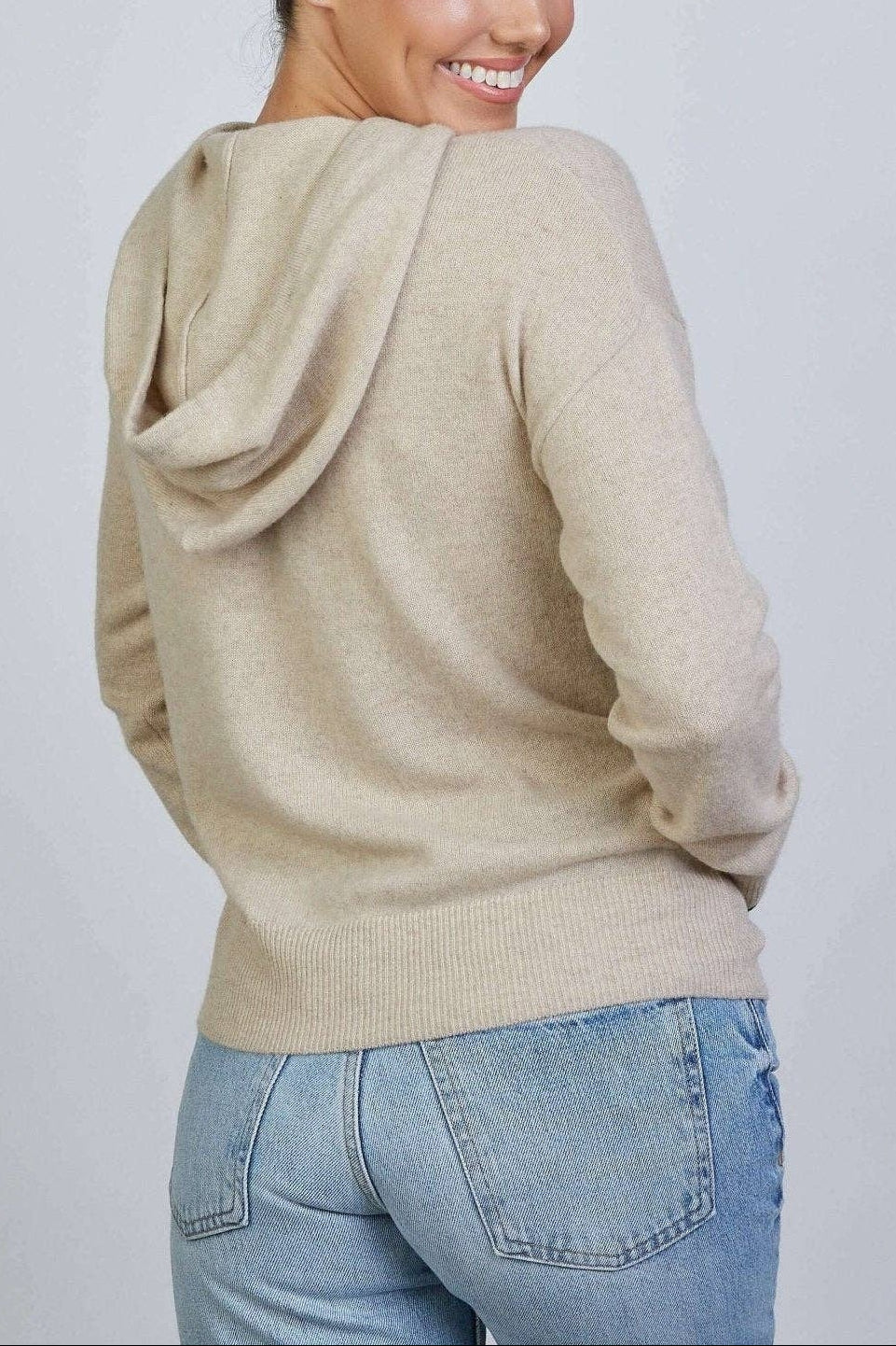 Woman wearing a beige hoodie and blue jeans on a plain background