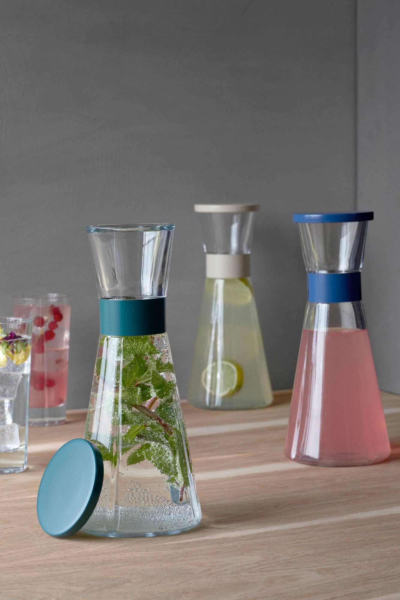 Set of glass carafes with colorful lids on a wooden surface.