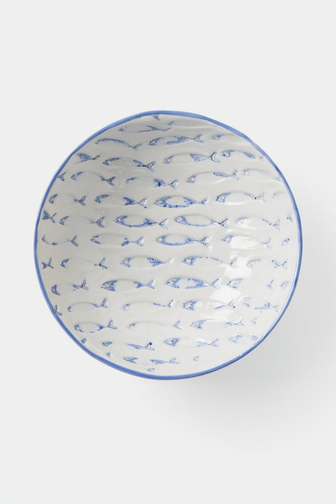 A white ceramic bowl with a blue painted pattern of small fish inside and a solid blue rim, shown from a top-down view on a light gray background.