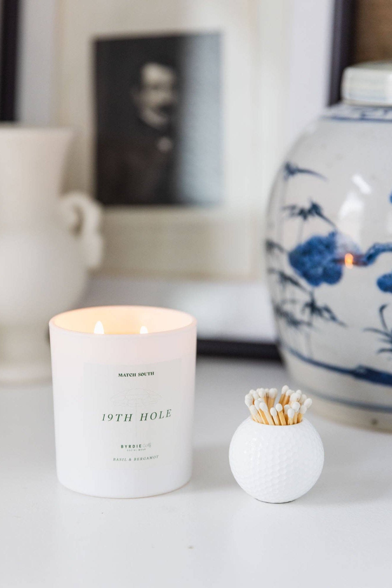 Candle labeled '19th Hole' with matches on a surface, with decorative items in the background.