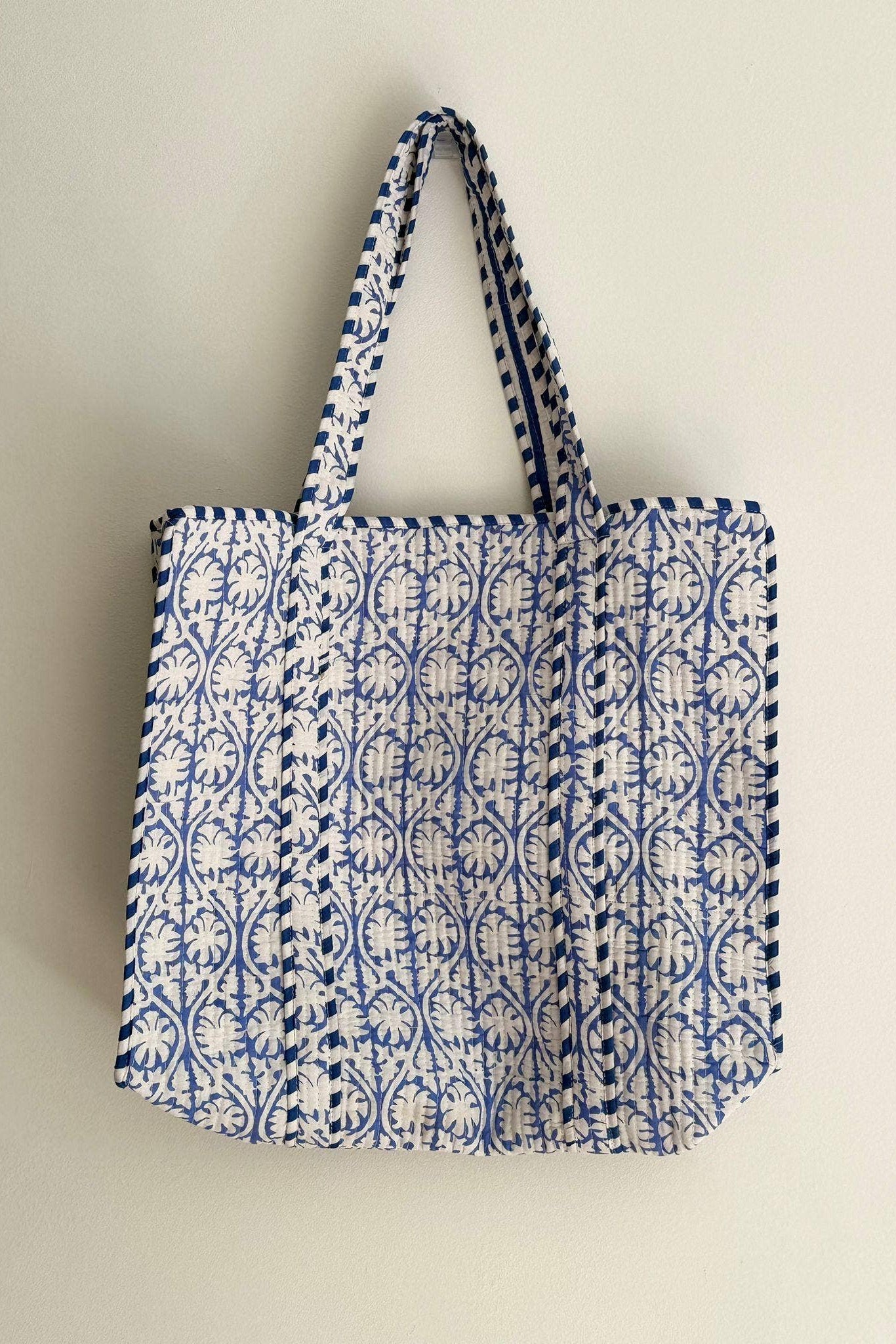 Blue and white patterned tote bag on a wooden table in a bright room with a couch and plants.