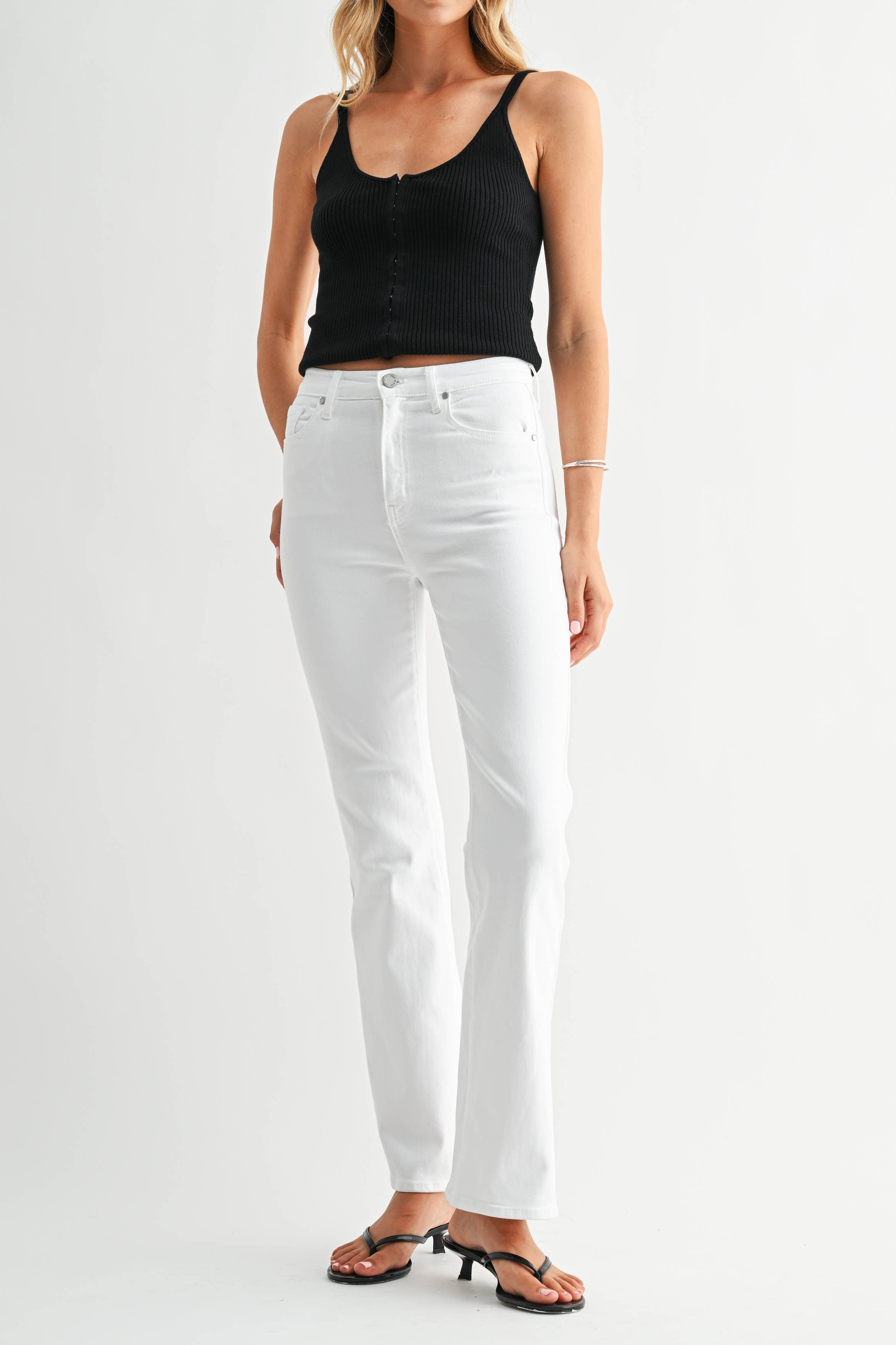 Woman wearing a black tank top and white jeans on a white background