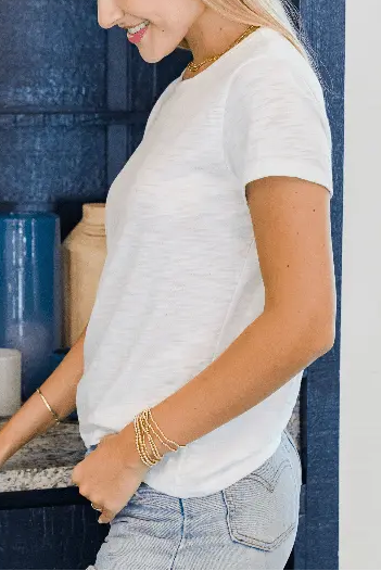 Woman in a white shirt and jeans standing in a room with blue walls and decorative mirror.