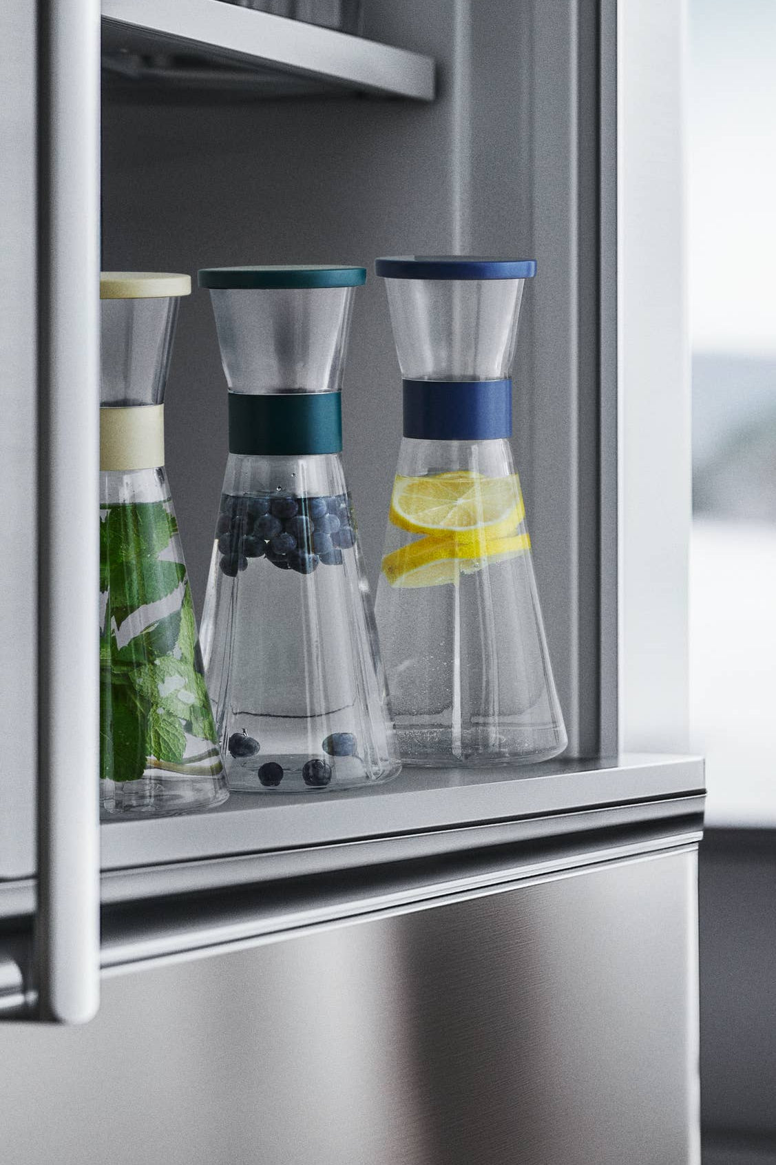 Clear glass carafes with colorful liquids inside a refrigerator.