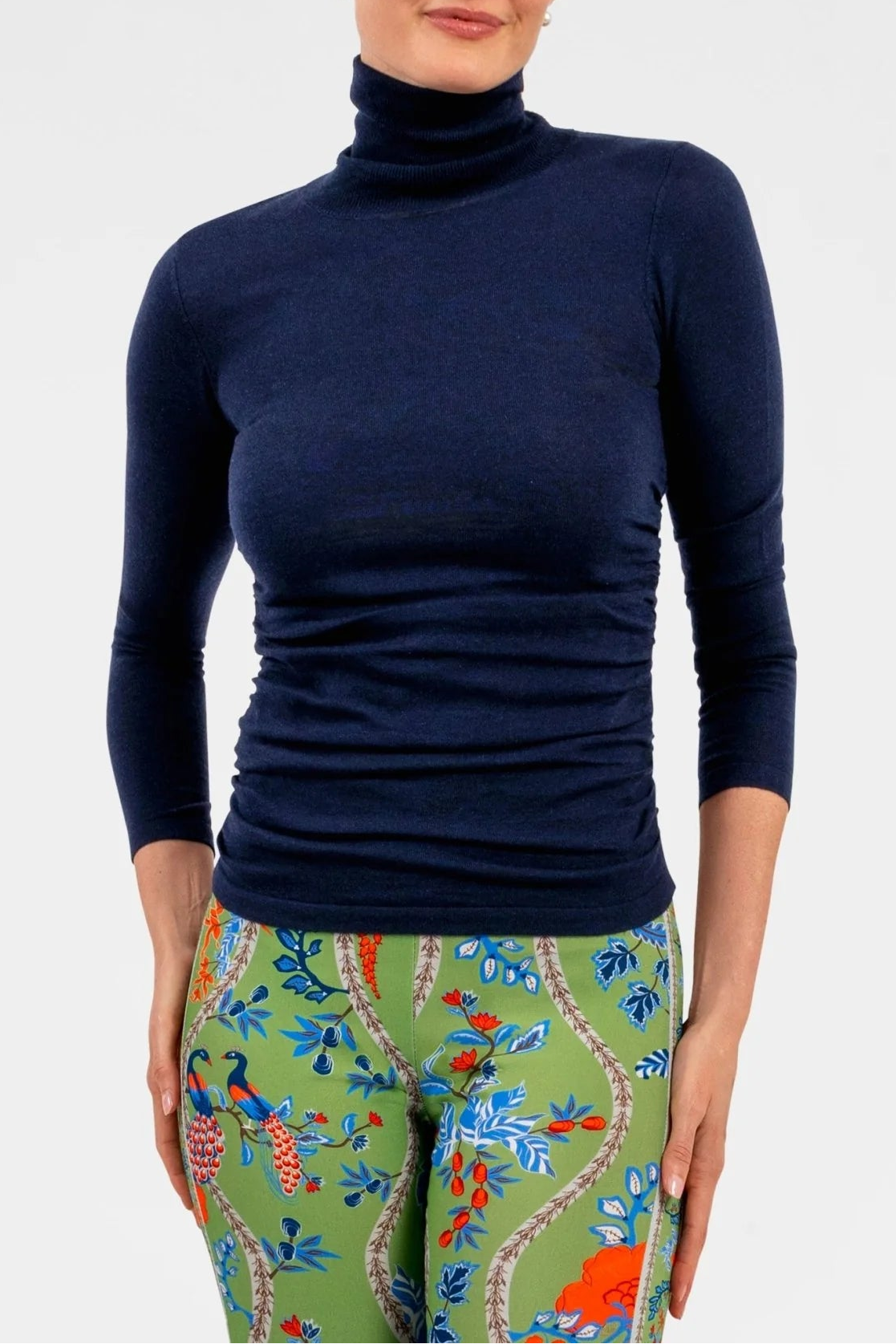 Woman wearing a navy turtleneck sweater and colorful patterned pants on a white background