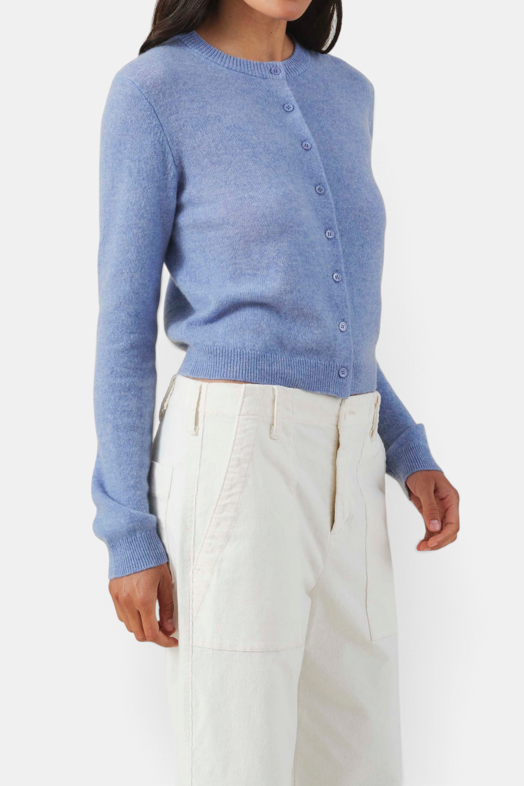 The Copper Shed blue cashmere cardigan with crew neck, button front, and ribbed trim worn with white trousers.