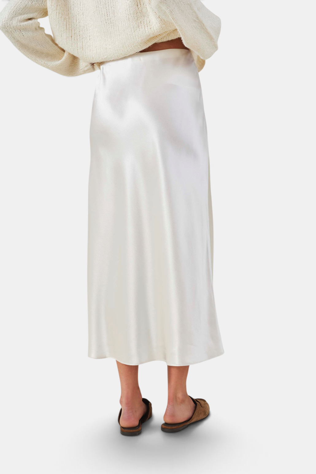 The Copper Shed Ella skirt in cream satin with a bias-cut silhouette and high-rise waist, worn with a knit sweater.