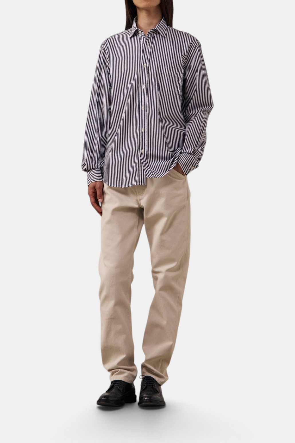 The Copper Shed Paul poplin striped cotton shirt with a semi-spread collar and button-front, worn with beige trousers.