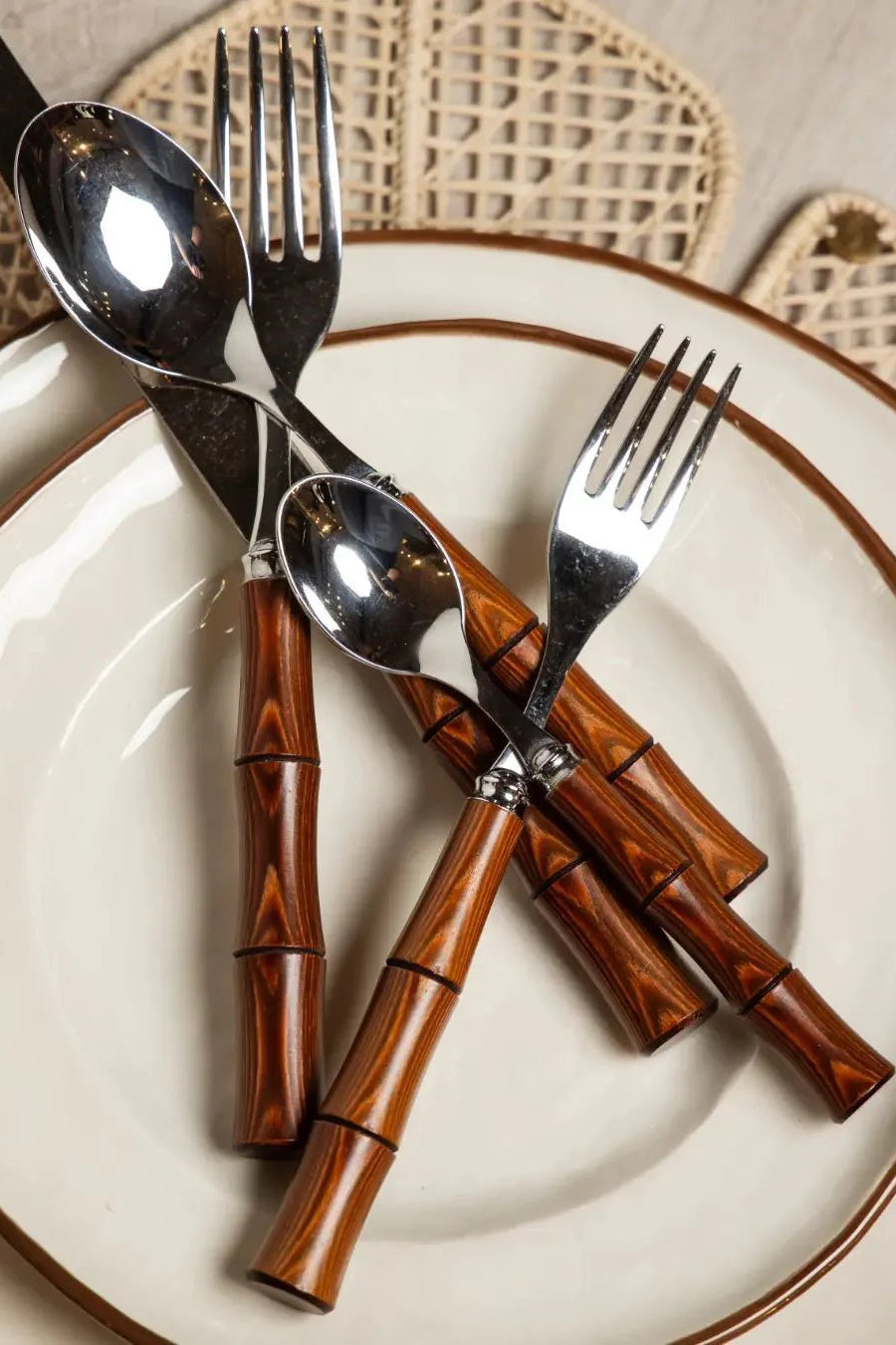 Silver cutlery with wooden handles on a white plate with a brown rim.