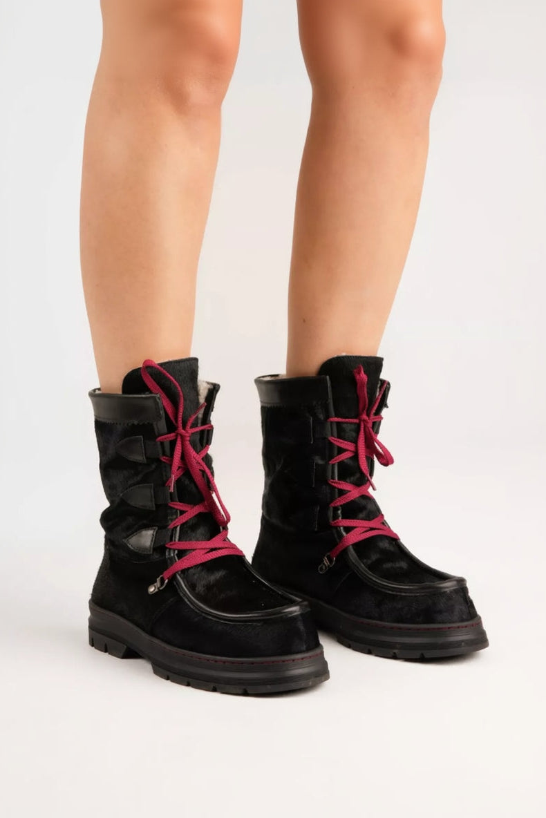 Black boots with red laces worn by a person on a white background