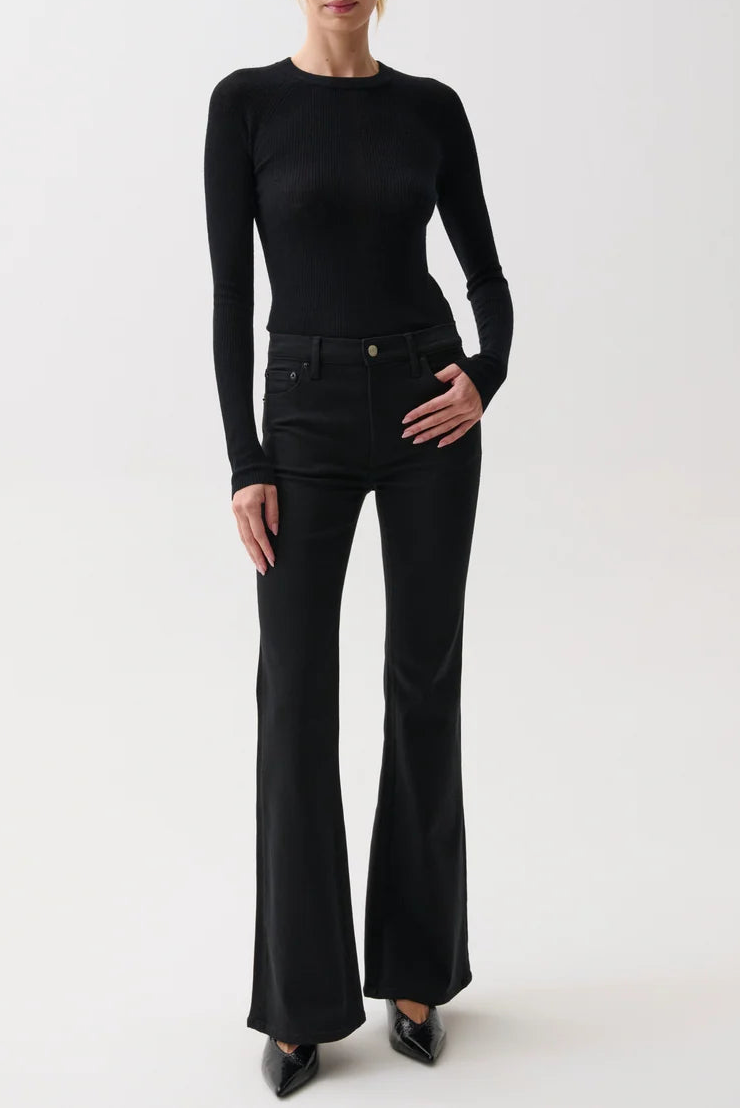 A woman modeling a black long-sleeve crewneck top and black flared pants against a plain light gray studio background.