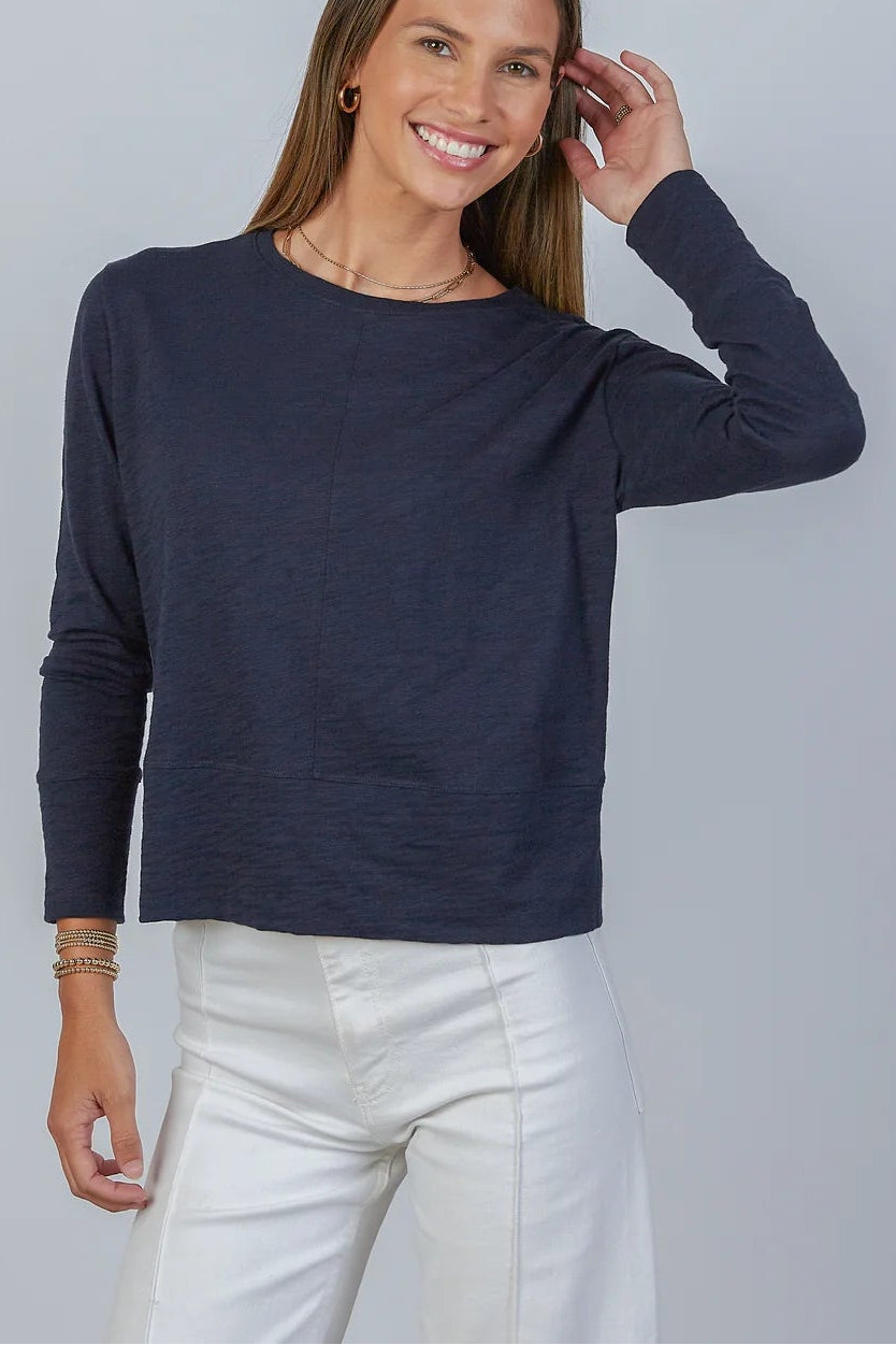 Woman wearing a navy blue sweater and white pants against a gray background