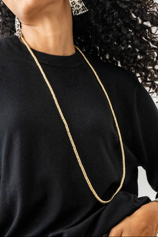 Woman wearing a black long-sleeve top with a gold necklace against a white background