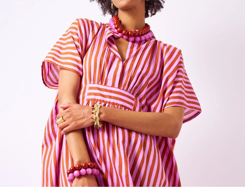 Woman wearing a pink and orange striped dress with jewelry on a white background