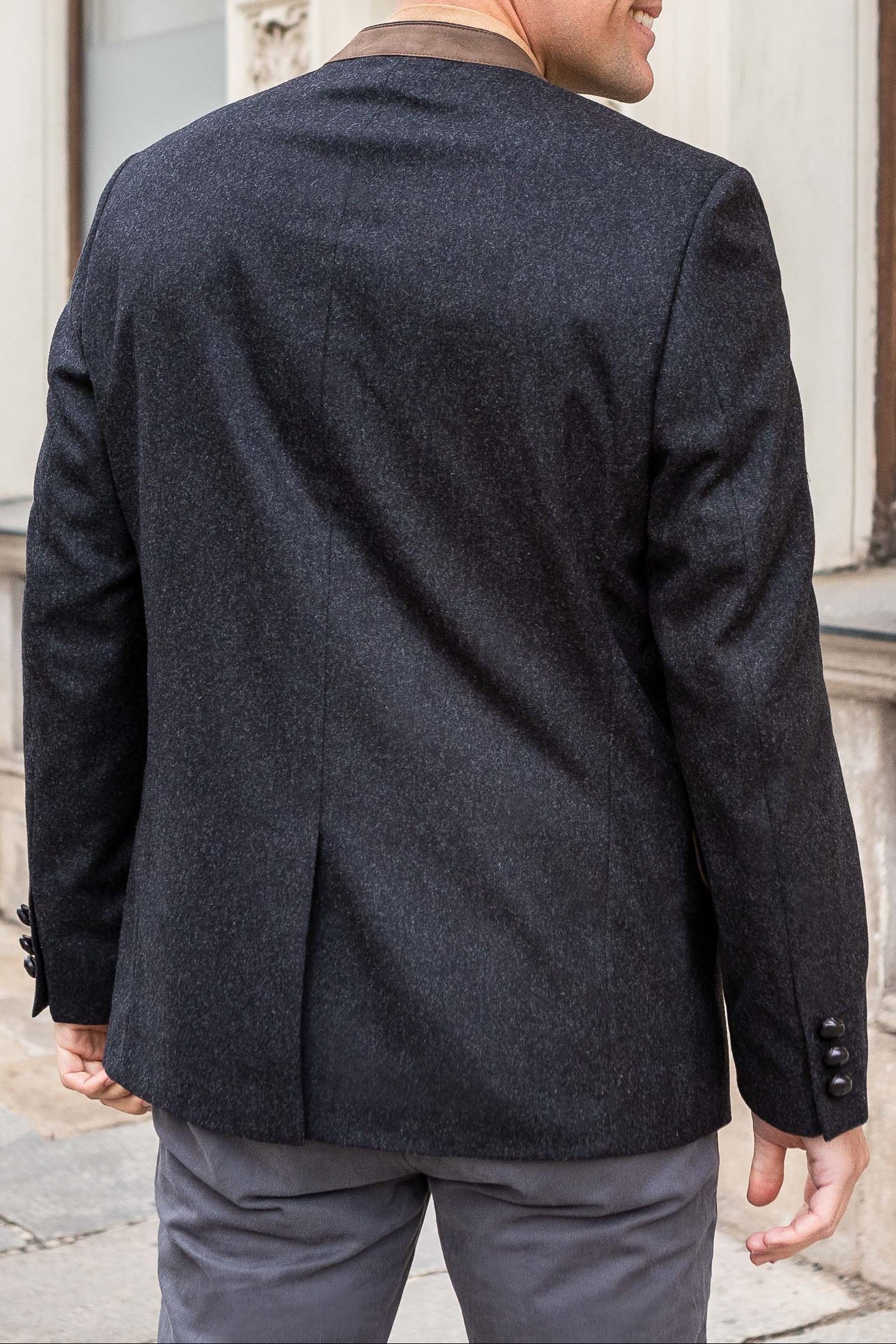 Man wearing a dark gray blazer and light gray pants standing in front of a building.
