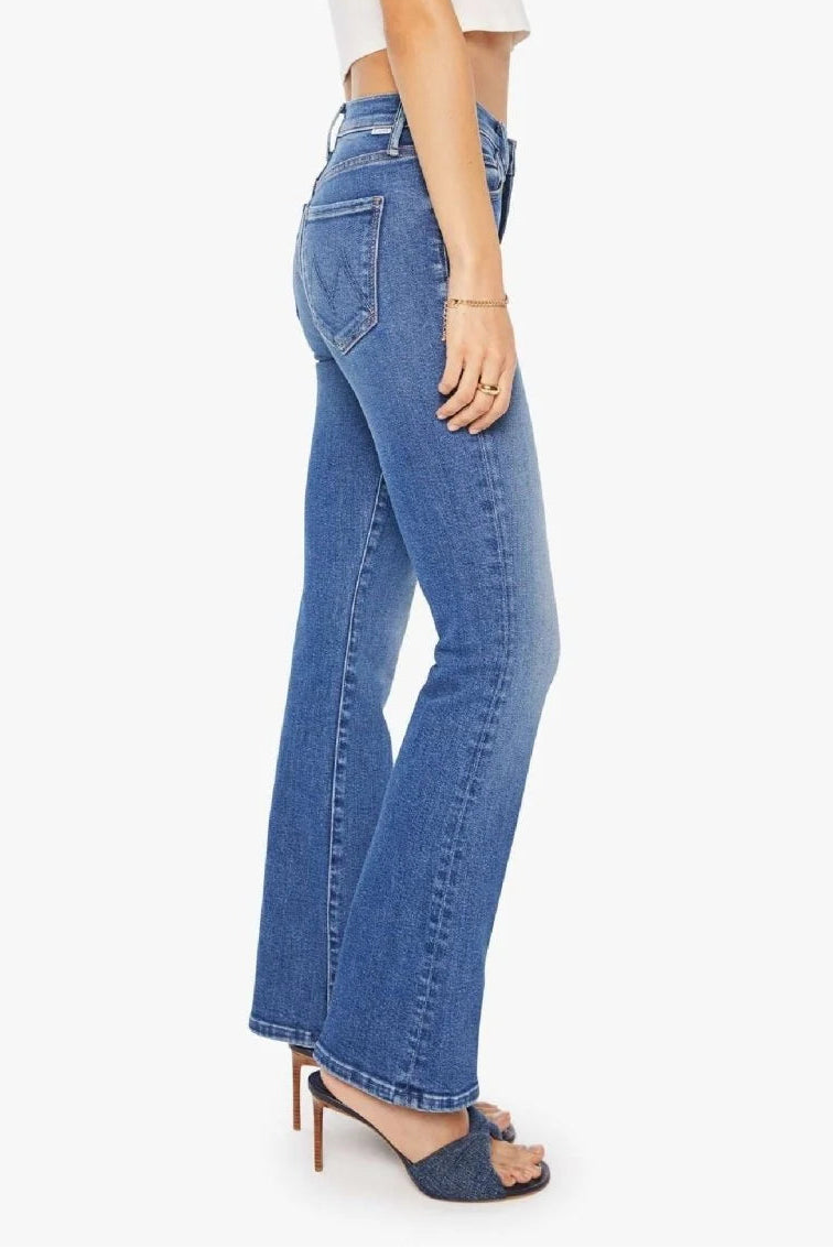 A side profile view of a model wearing blue high-waisted flare jeans, styled with a white cropped top and dark blue heeled sandals against a light gray background.