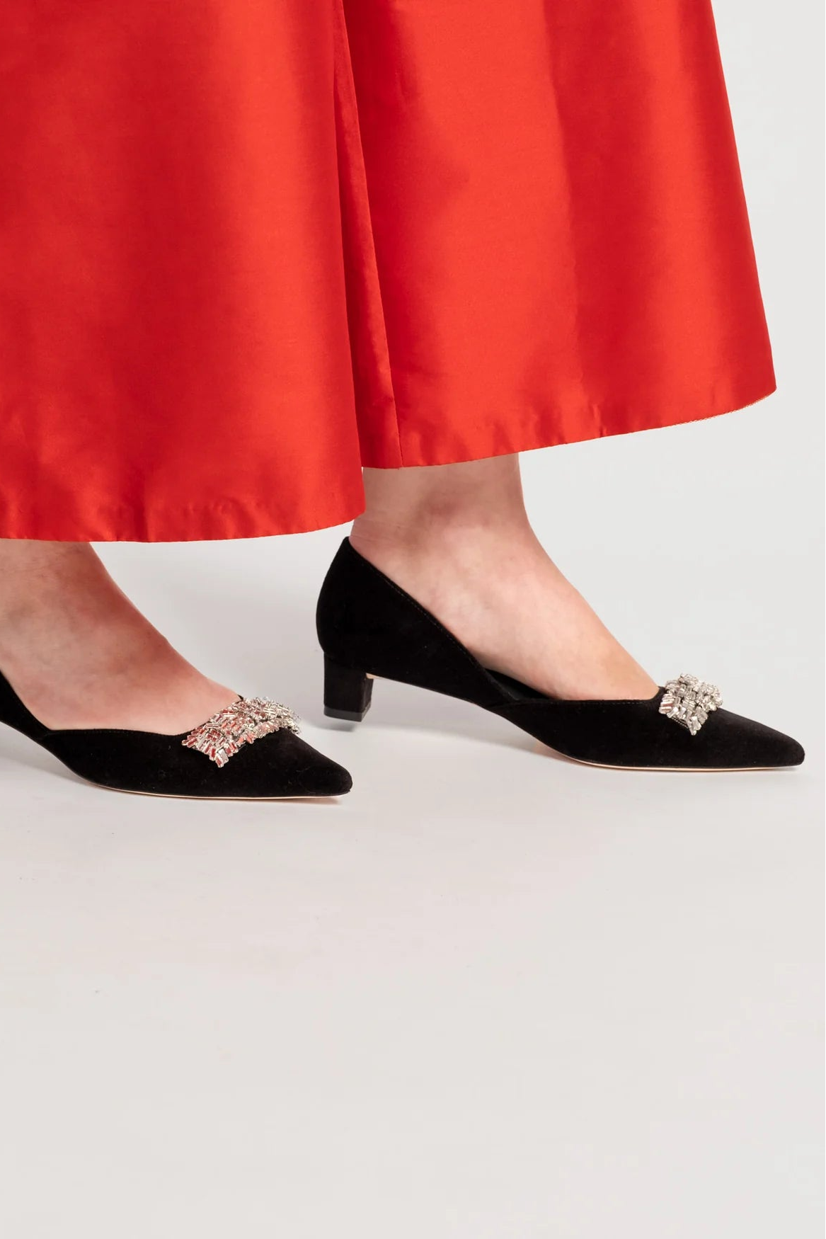 Black shoes with embellishments worn with red pants on a light background