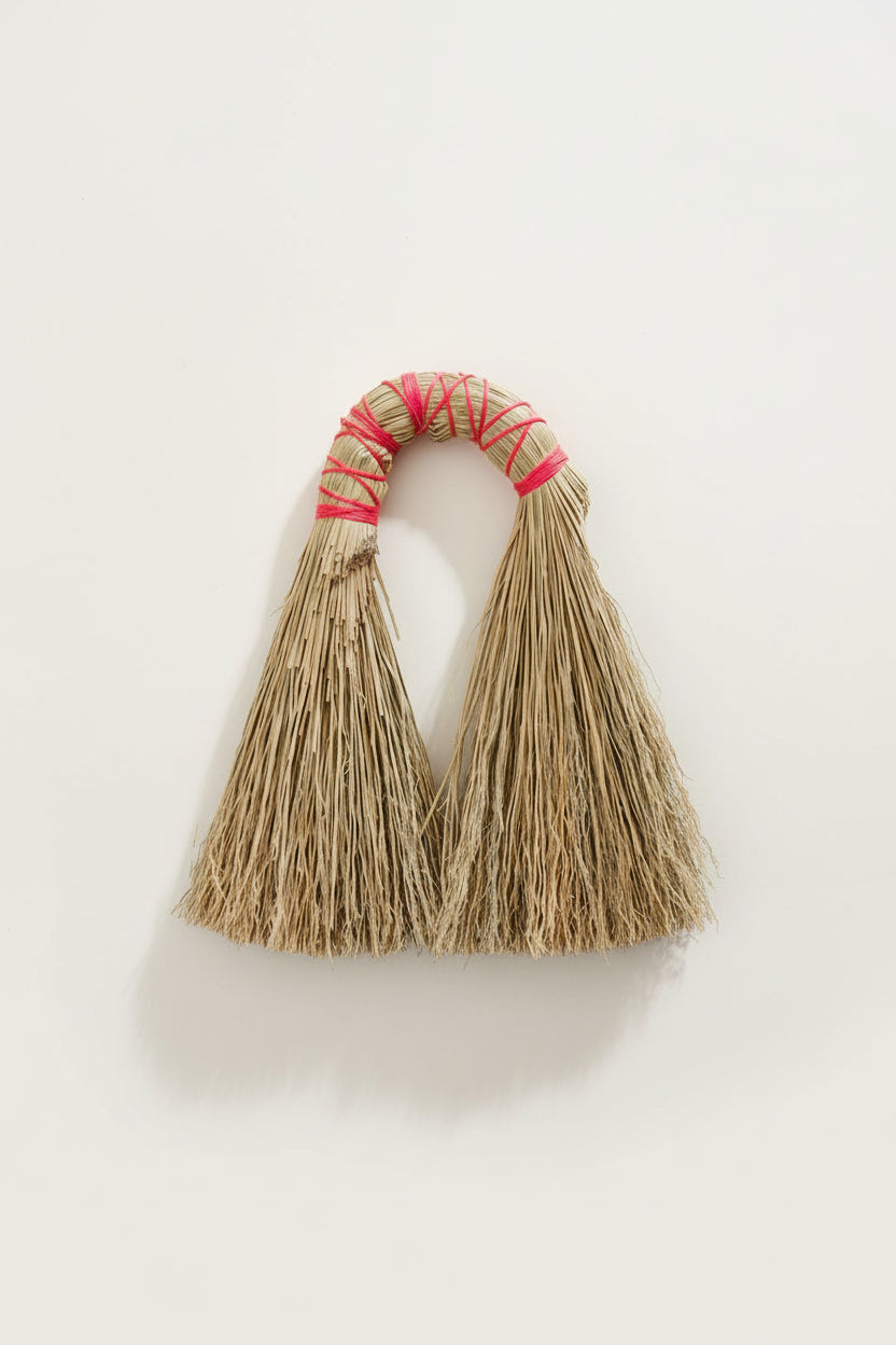 Bamboo tassels with pink thread on a wooden block surrounded by dry grass.