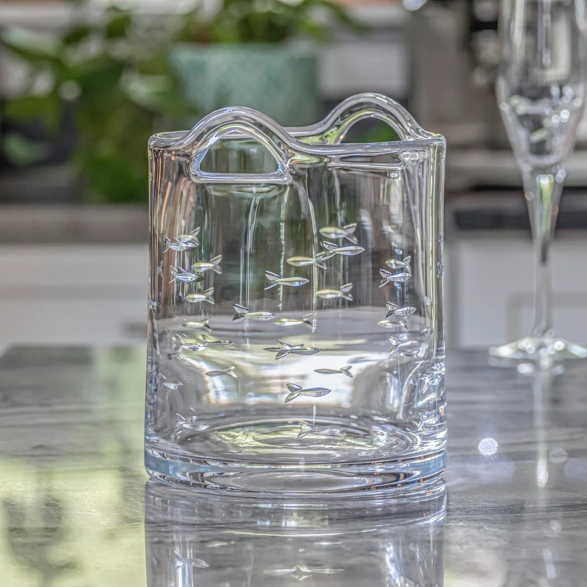 Clear glass vase with fish patterns on a reflective surface