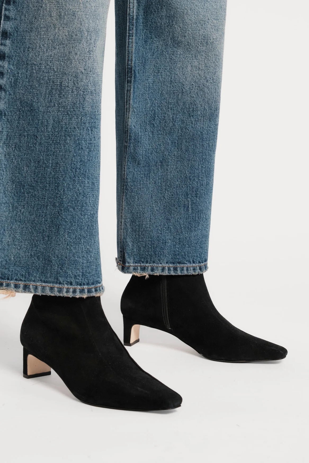 Black pointed-toe ankle boots with a block heel, worn with light-wash blue jeans against a plain light gray studio background.
