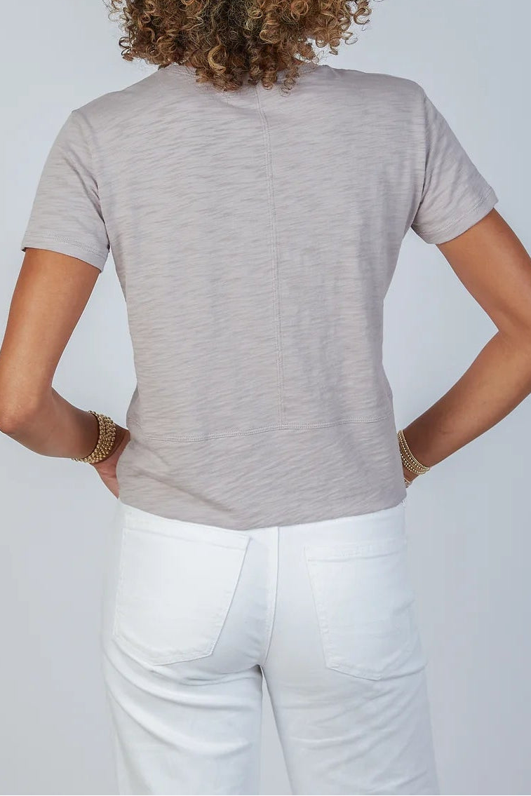 Person wearing a gray t-shirt and white pants against a plain background