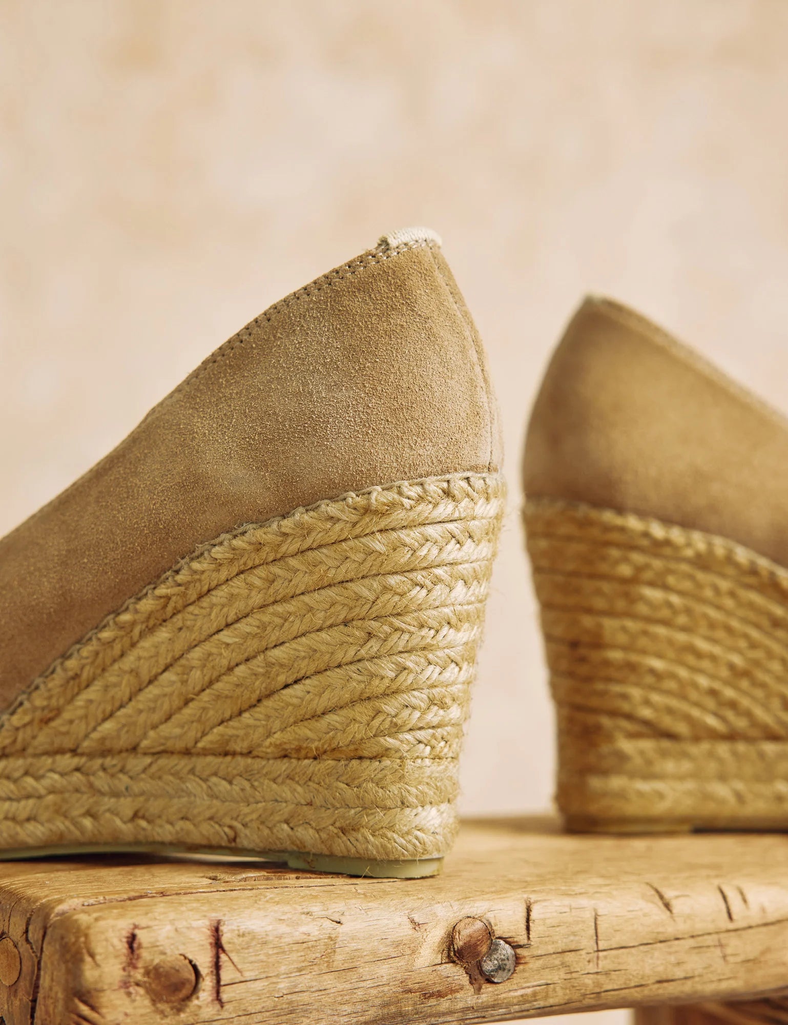 Pair of beige wedge sandals with woven soles on a wooden surface.