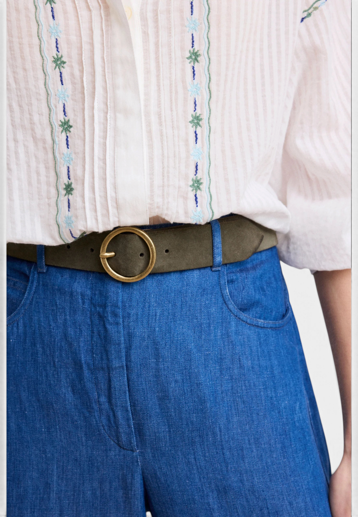 The Copper Shed Aronde women's belt in olive green suede with a round gold buckle worn over blue denim trousers
